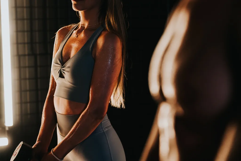 Woman lifting a dumbbell beside a blurred male form in a dimly lit studio